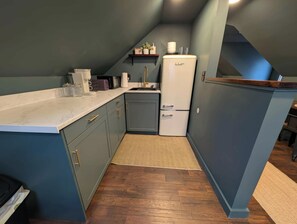 Eine kleine Küche mit integriertem Kühlschrank, Spüle und Arbeitsplatte, ausgestattet mit verschiedenen Geräten.