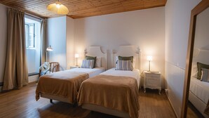 A hotel room with two beds, wooden flooring, a ceiling with wooden beams, and a large window with curtains. - Vrbo Property (Rabo de Peixe)
