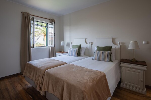 A double room with two beds, a window with curtains, bedside lamps, and a nightstand.