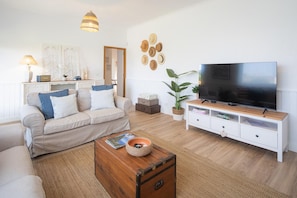 A living room with a sofa, a coffee table, a television, and a wall with decorative items.