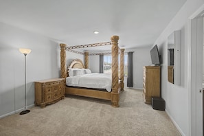 A four-poster bed with a canopy, a wooden dresser, a television on a stand, and a floor lamp.
