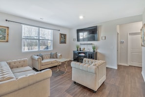 A living room with a sofa, armchairs, a coffee table, and a flat-screen TV mounted on the wall.