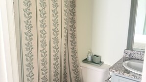 Un bany amb vàter, cortina de bany amb dibuixos florals, un rentapeus amb taulell de granat i un mirall.
