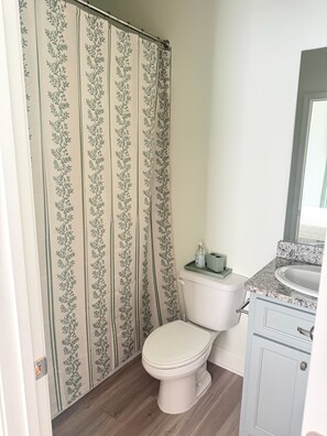 Een badkamer met toilet, douchegordijn met bloemenprint, wastafel met granieten blad en een spiegel.