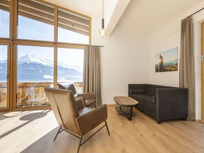 Ein modernes Wohnzimmer mit Blick auf einen verschneiten Berg, einer Couch, einem Sessel und einem kleinen Tisch.