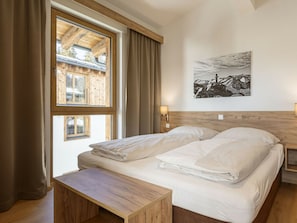 Ein Schlafzimmer mit einem Bett, einem Nachttisch, einem Fenster mit Vorhängen und einer Wandlampe.