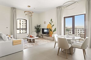 A modern living room with a sofa, a coffee table, a TV, and a dining area with chairs and a table. - Silkhaus NEW Luxurious 1BR in Yas Golf Collection (Abu Dhabi)