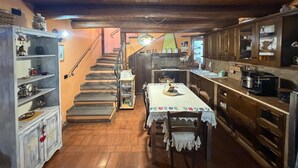 A rustic kitchen with wooden cabinets, a dining table with a lace tablecloth, and a staircase leading to an upper level. - Quaint 1-bedroom house in lovely Sugano perfect for relaxing stays (Sugano)