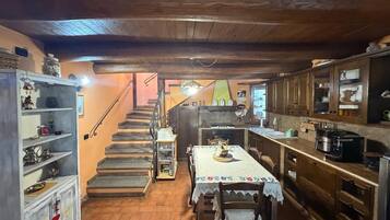 A rustic kitchen with wooden cabinets, a dining table with a lace tablecloth, and a staircase leading to an upper level.