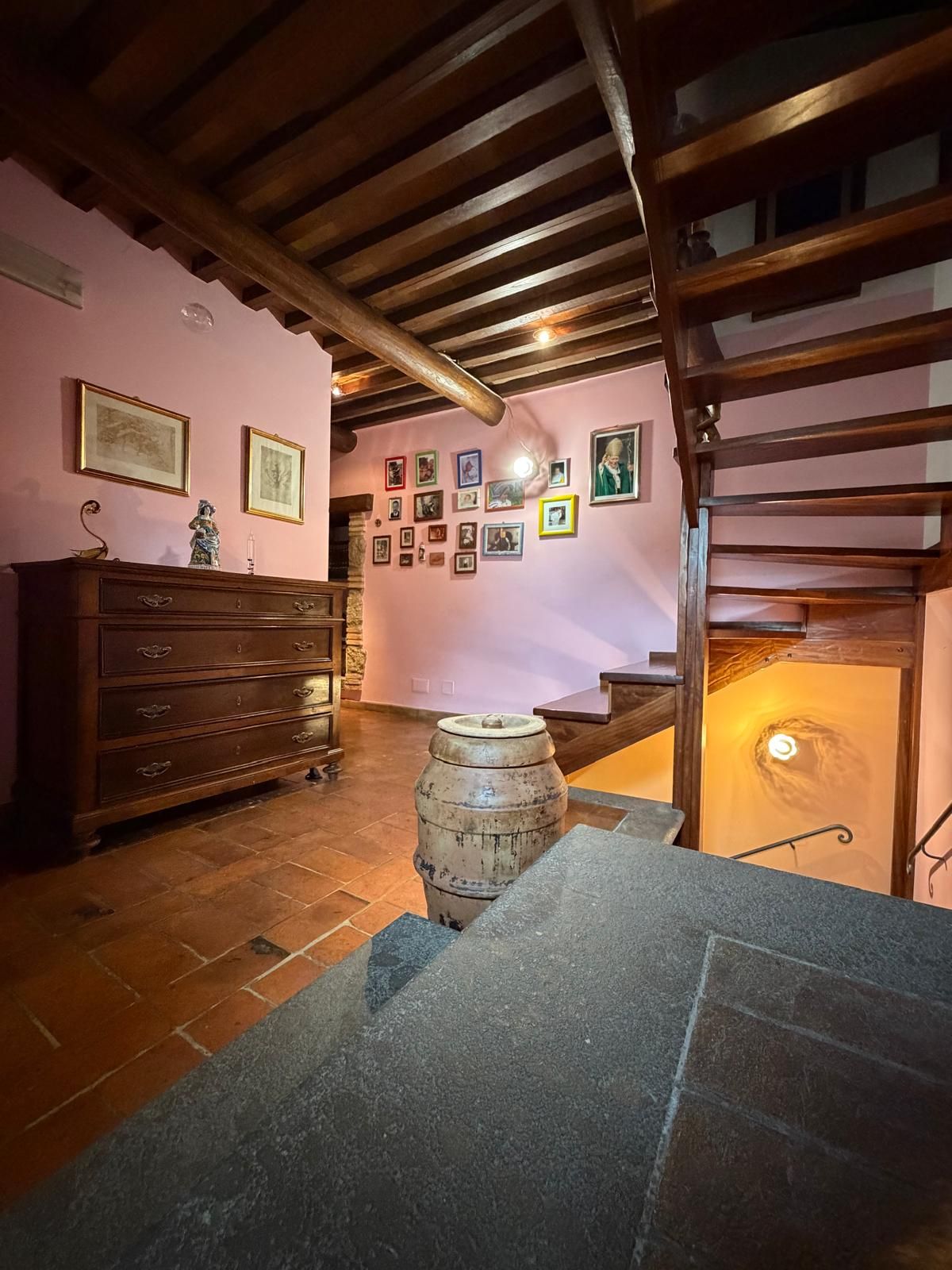 Una habitación con techo de madera, chimenea de piedra, cómoda de madera y una pared decorada con cuadros.