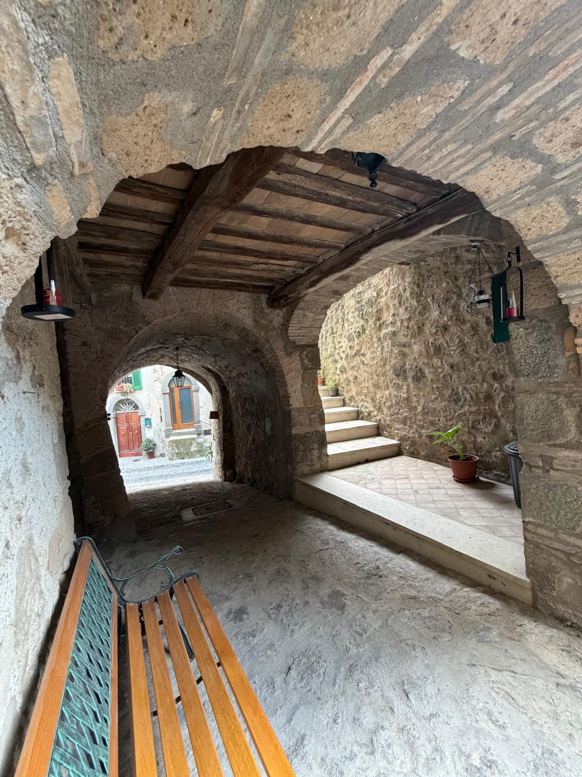 Ein Innenraum mit einer hölzernen Bank, Steinwänden, einer Treppe und Blick auf eine Straße.