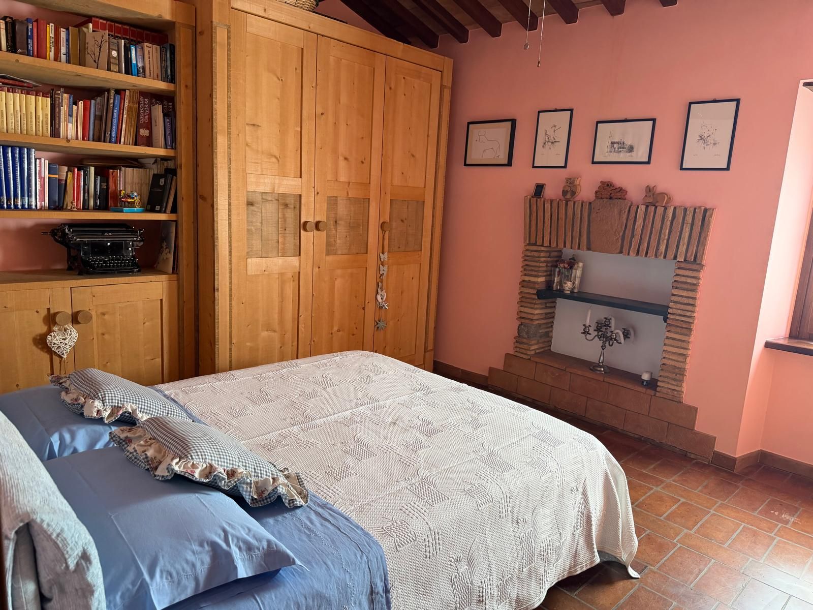 A bedroom with a bed, a wooden wardrobe, a bookshelf, and a fireplace.