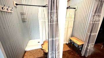 Un baño con cortina de ducha, un banco y un perchero.