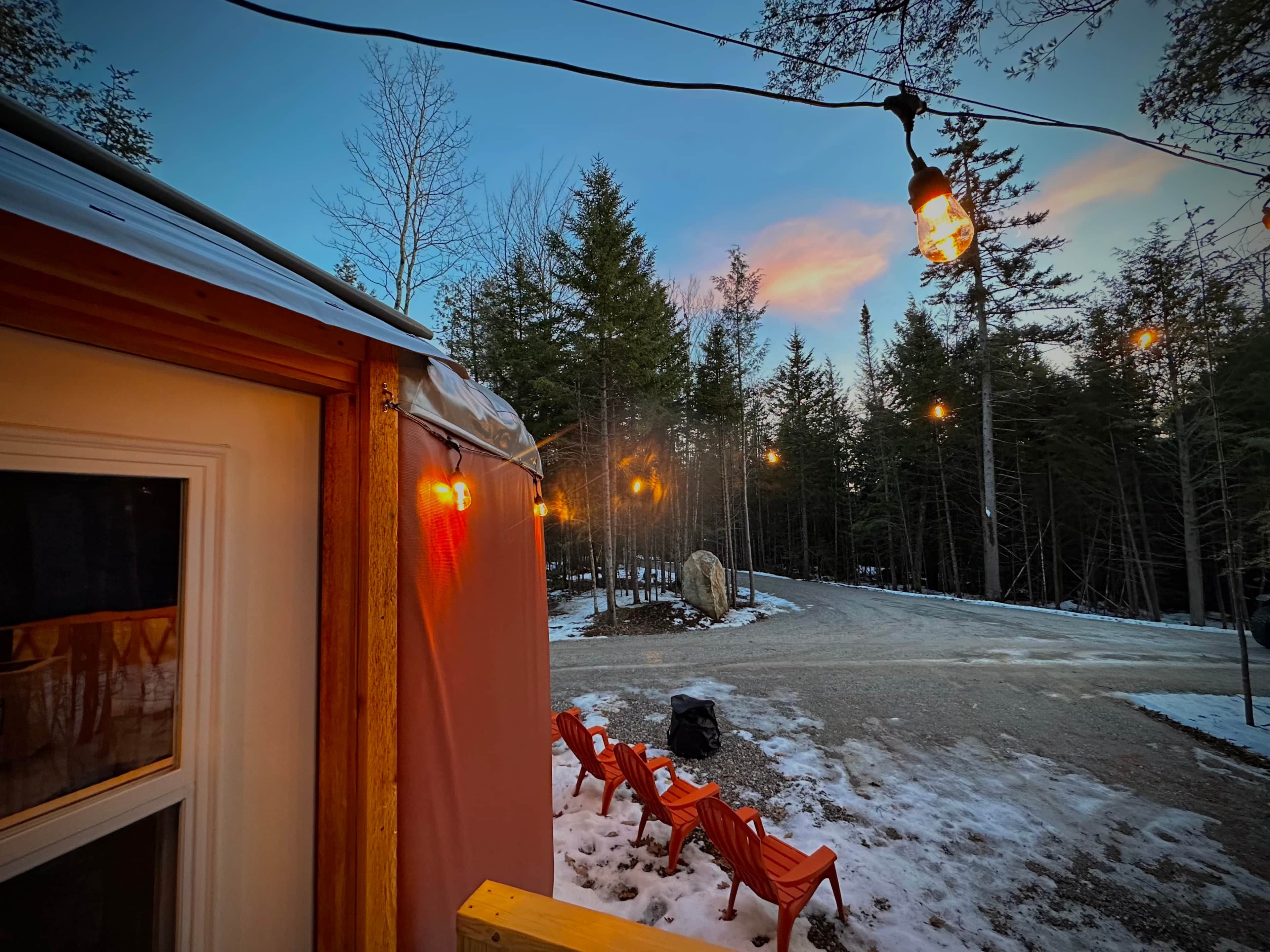 A wooden building with a window, outdoor seating with chairs, and a snow-covered ground.