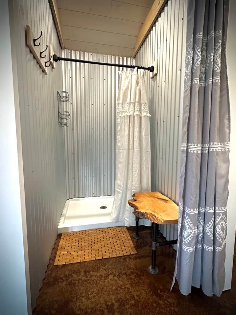 Ein kleines Badezimmer mit Dusche, einem hölzernen Hocker und einem Handtuchhalter.