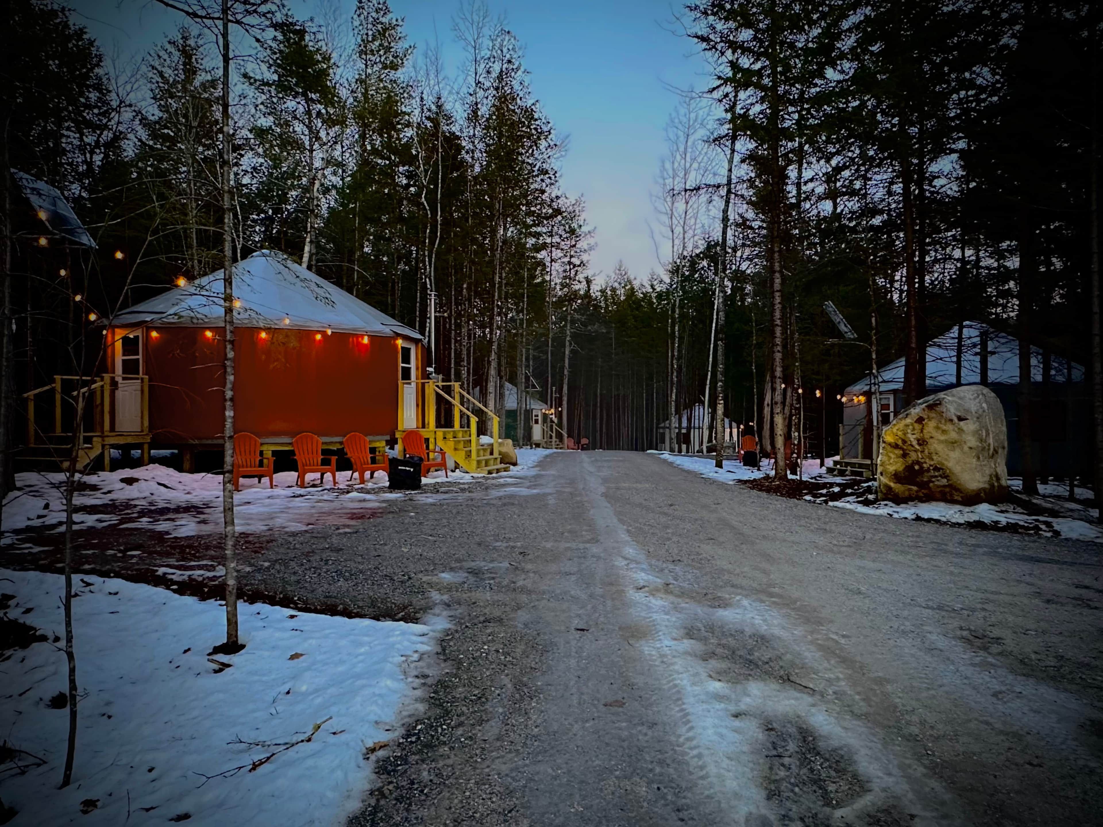 Un camino cubierto de nieve que conduce a una cabaña con un porche y mobiliario exterior.