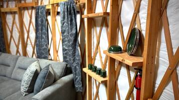 Ein gemütliches Zimmer mit sichtbarer Holzbalkendecke, einem grauen Sofa und Regalen mit grünen Geschirrgegenständen sowie einem Feuerlöscher.