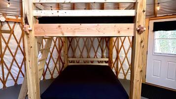 A bunk bed with a wooden frame and a black mattress, set against a backdrop of a tent-like structure with a lattice design.