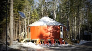 Eine Jurte mit Solarpanel, umgeben von Bäumen, mit Sitzgelegenheit im Freien.