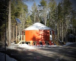 A yurt with a solar panel, surrounded by trees, with outdoor seating. - The Cupsuptic Glamping Yurt in Bethel, Maine (Bethel)