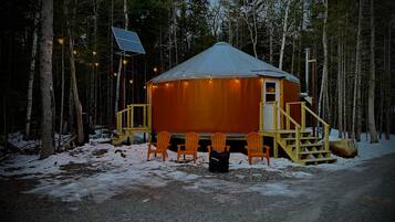 En stuga med ett snötäckt tak, omgiven av en skog. Det finns en trappa av trä som leder upp till ingången, och en solpanel syns på taket.