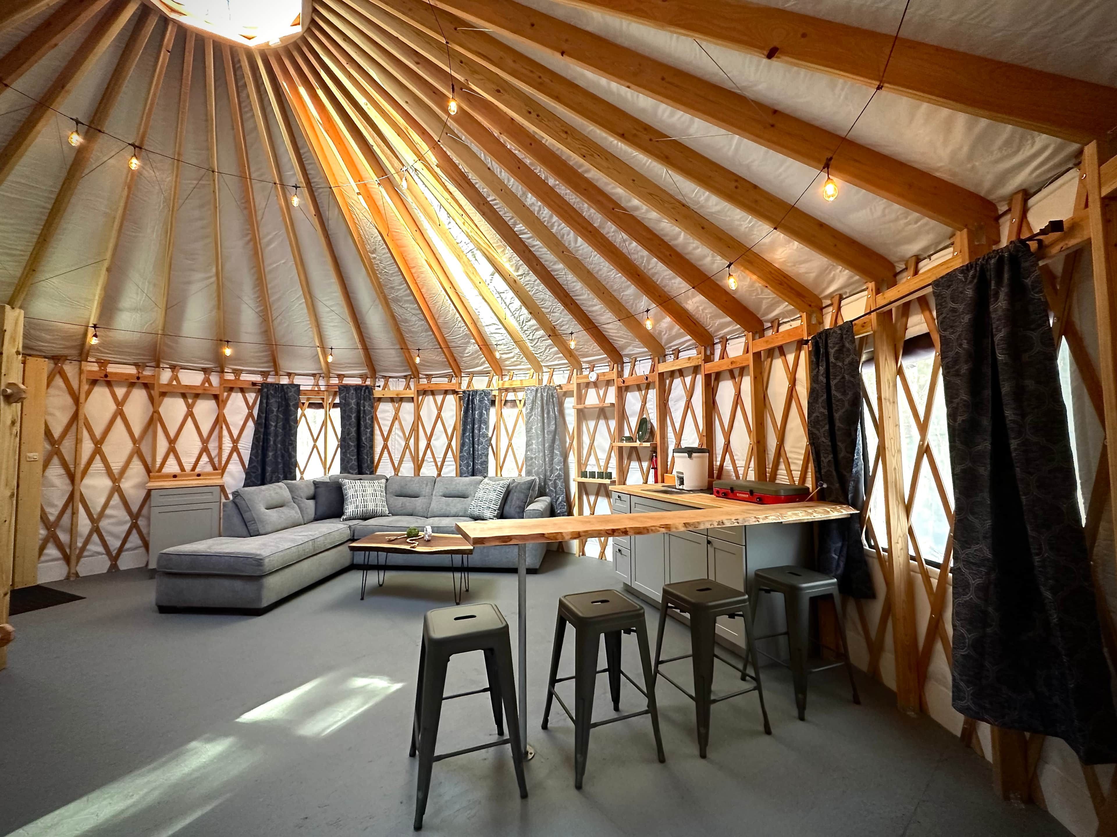 A yurt interior with a sofa, dining table, stools, and a kitchen area.