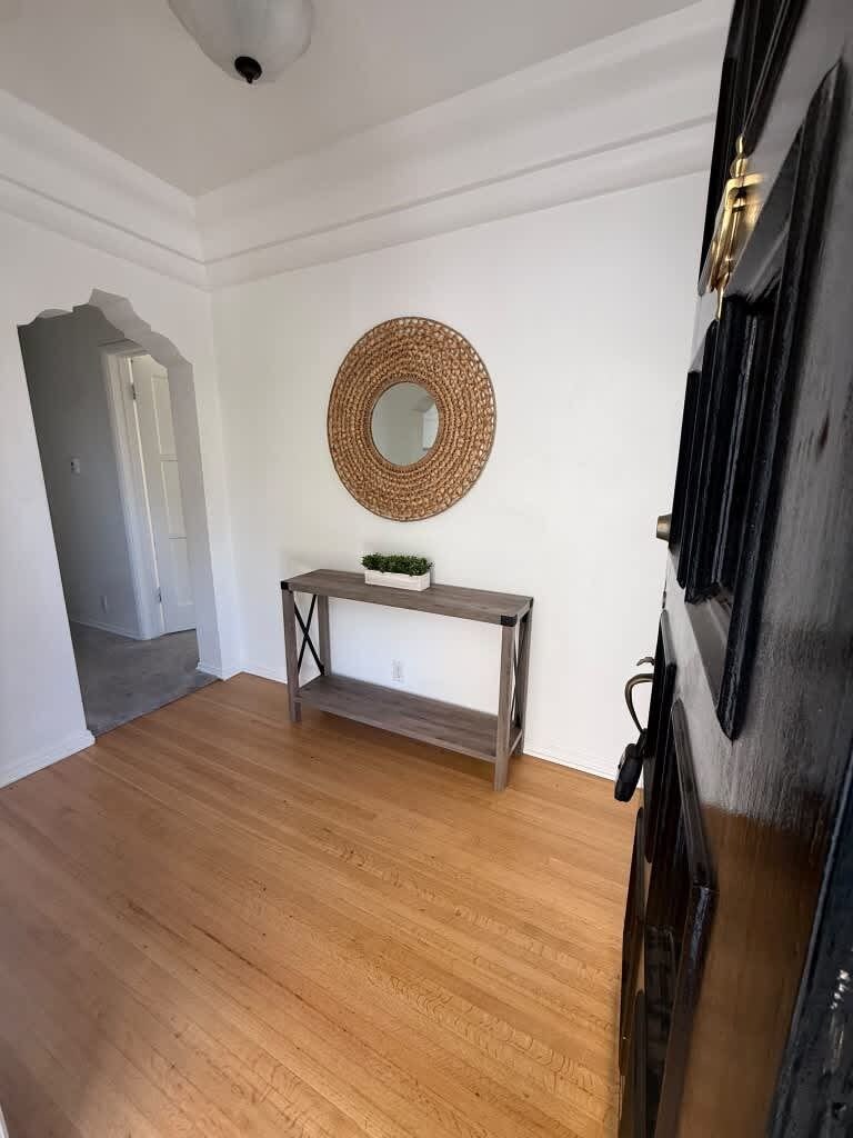 A room with a wooden floor, a round mirror on the wall, a small table with a plant, and a door with a black frame.
