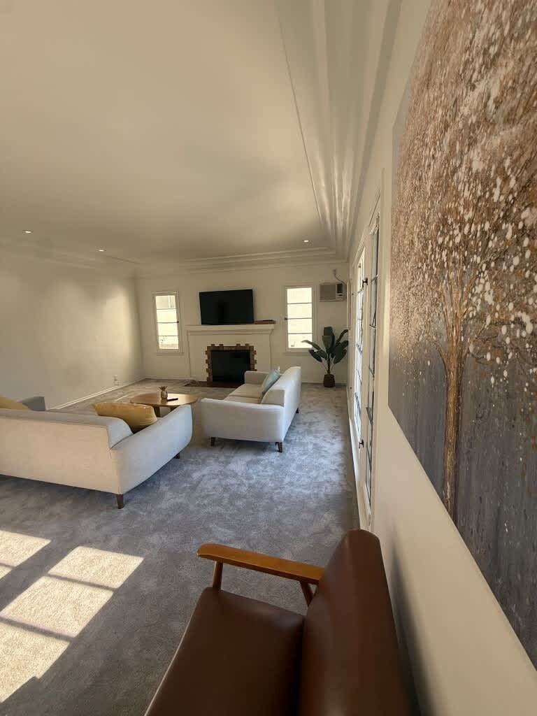 Uma sala de estar ampla com uma pintura grande, uma lareira e uma TV de tela plana.