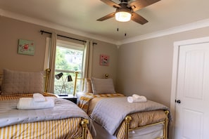 Un dormitorio con dos camas, ventilador de techo y ventana con cortinas.