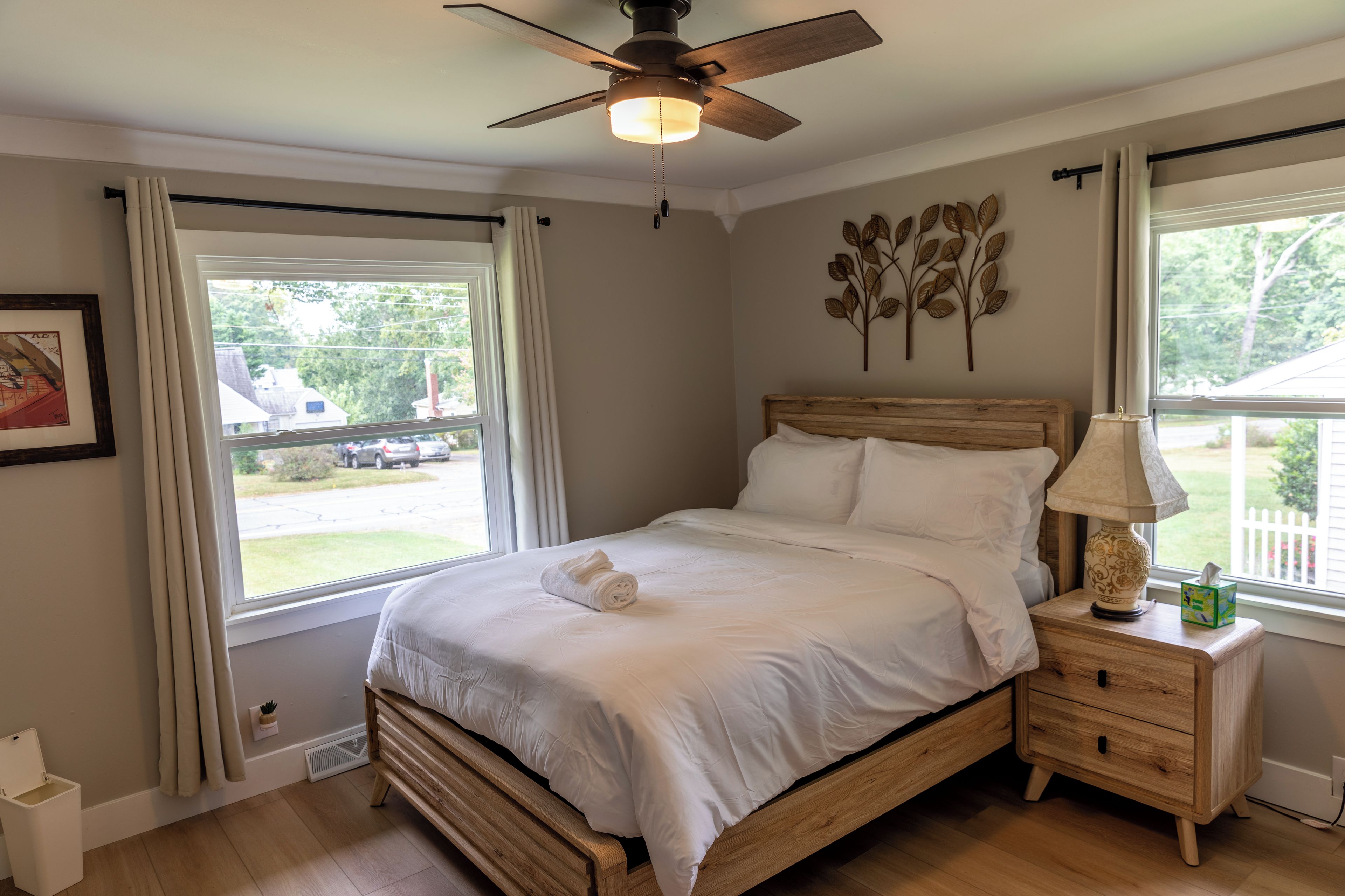Ein Schlafzimmer mit einem hölzernen Bett, weißer Bettwäsche, einem Deckenventilator und einem Fenster mit Vorhängen.