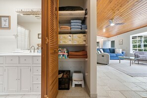 A laundry room with a wooden door, shelves with folded towels, and a small stool. - Charming 3-bedroom house with heated pool and within 5 miles from the beach. (Vero Beach)