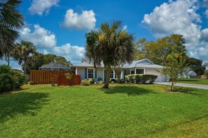A residential house with a well-maintained lawn, a wooden fence, and a palm tree. - Charming 3-bedroom house with heated pool and within 5 miles from the beach. (Vero Beach)