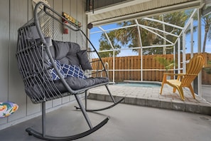 A rocking chair with cushions and a yellow chair by a pool. - Charming 3-bedroom house with heated pool and within 5 miles from the beach. (Vero Beach)