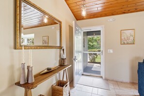 Un corridoio con soffitto in legno, un grande specchio, un consolle in legno con candele, una porta che dà sull'esterno e un quadro appeso al muro.