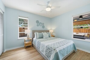 Una camera da letto con un letto, comodini, una ventola a soffitto e una finestra vista su un pontile in legno.