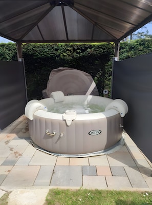 A hot tub under a covered patio with a stone-tiled floor and a hedge in the background. - Holiday Home 'Gîte Bord De Mer' with Sea View, Private Terrace and Wi-Fi (Petit-Caux)