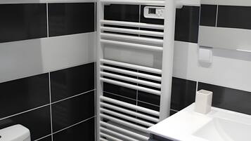 Ein Badezimmer mit einem weißen Waschbecken, schwarz-weißen Fliesen und einer weißen Toilette. Ein Handtuchhalter mit gefalteten Handtüchern ist ebenfalls vorhanden.