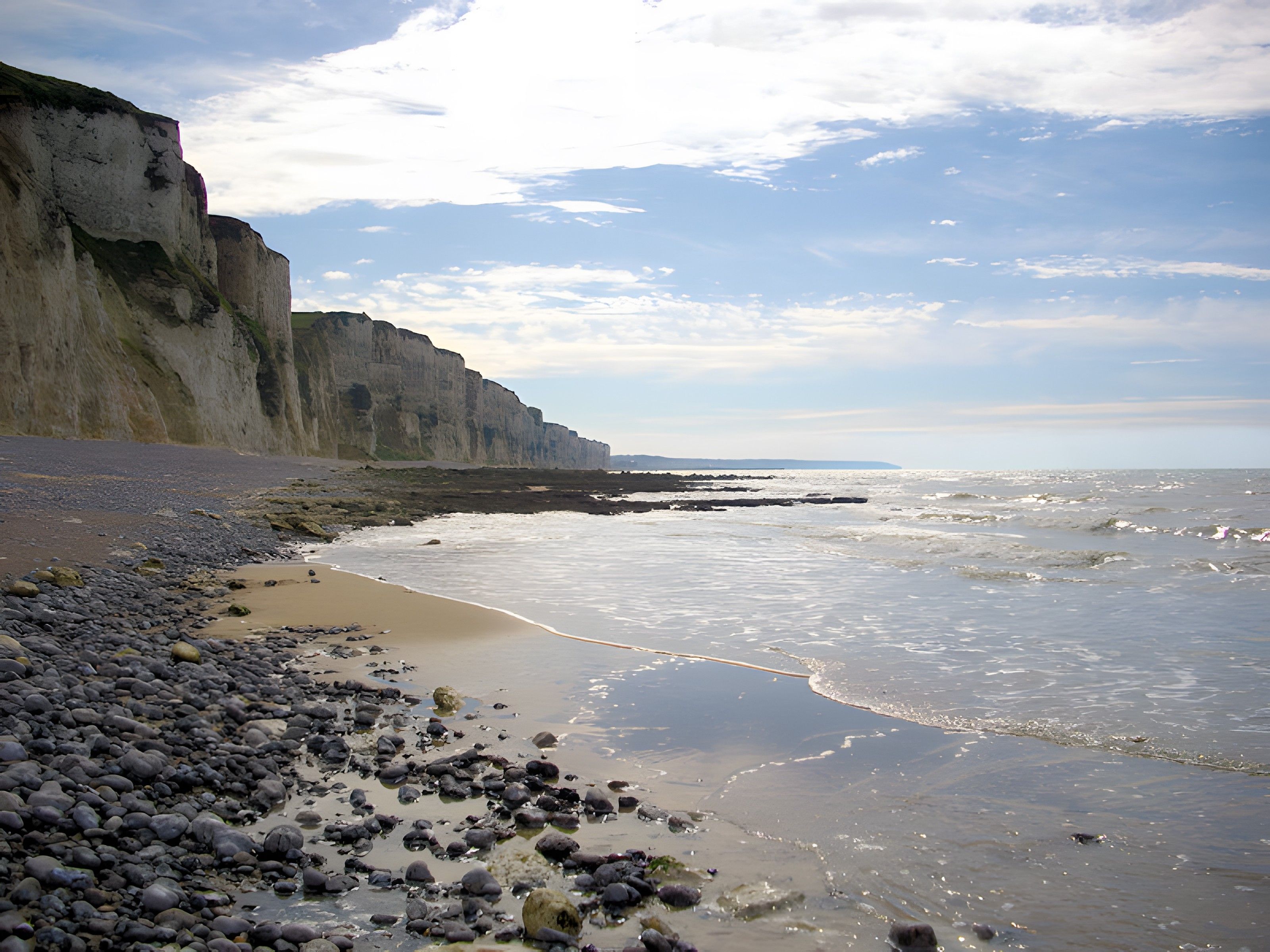 A coastal landscape with a rocky beach, cliffs, and a calm sea.
