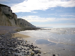 A coastal landscape with a rocky beach, cliffs, and a calm sea.