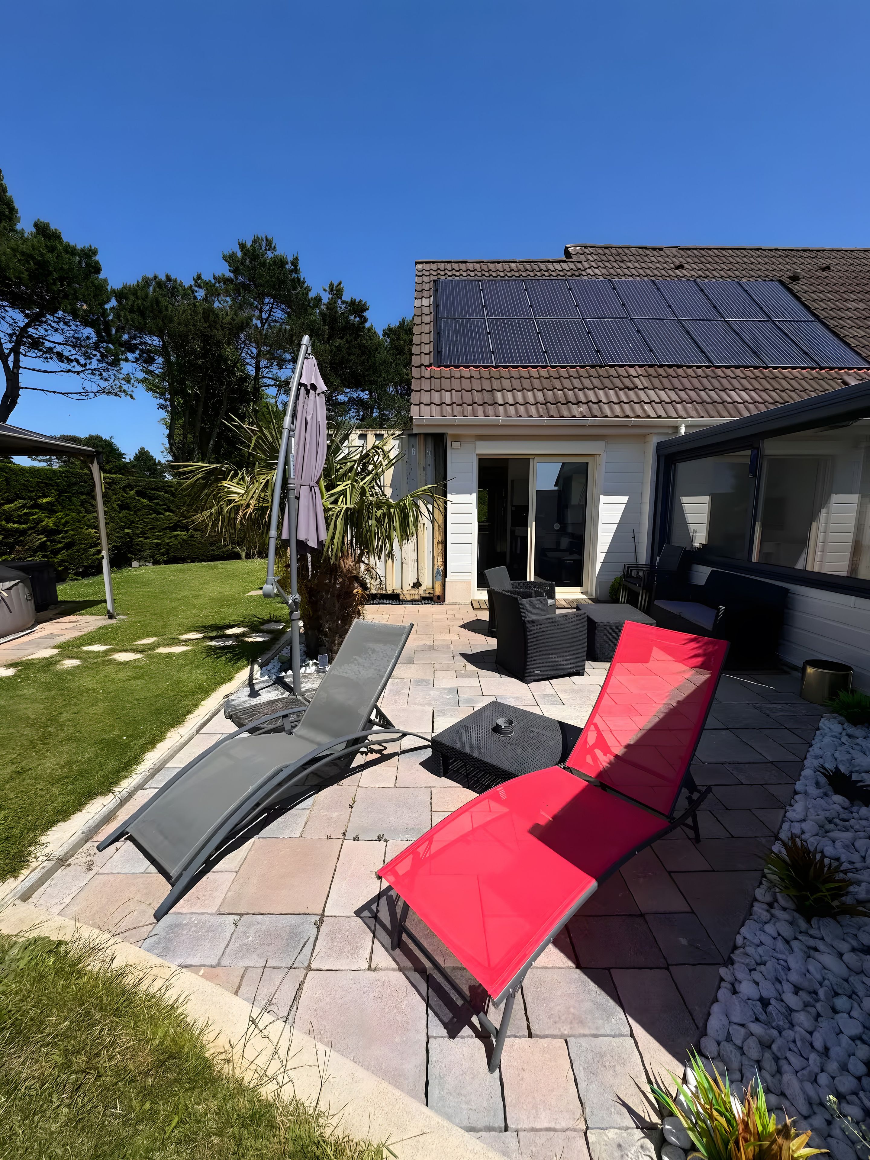 A patio area with outdoor furniture, a pergola, and a house with solar panels.