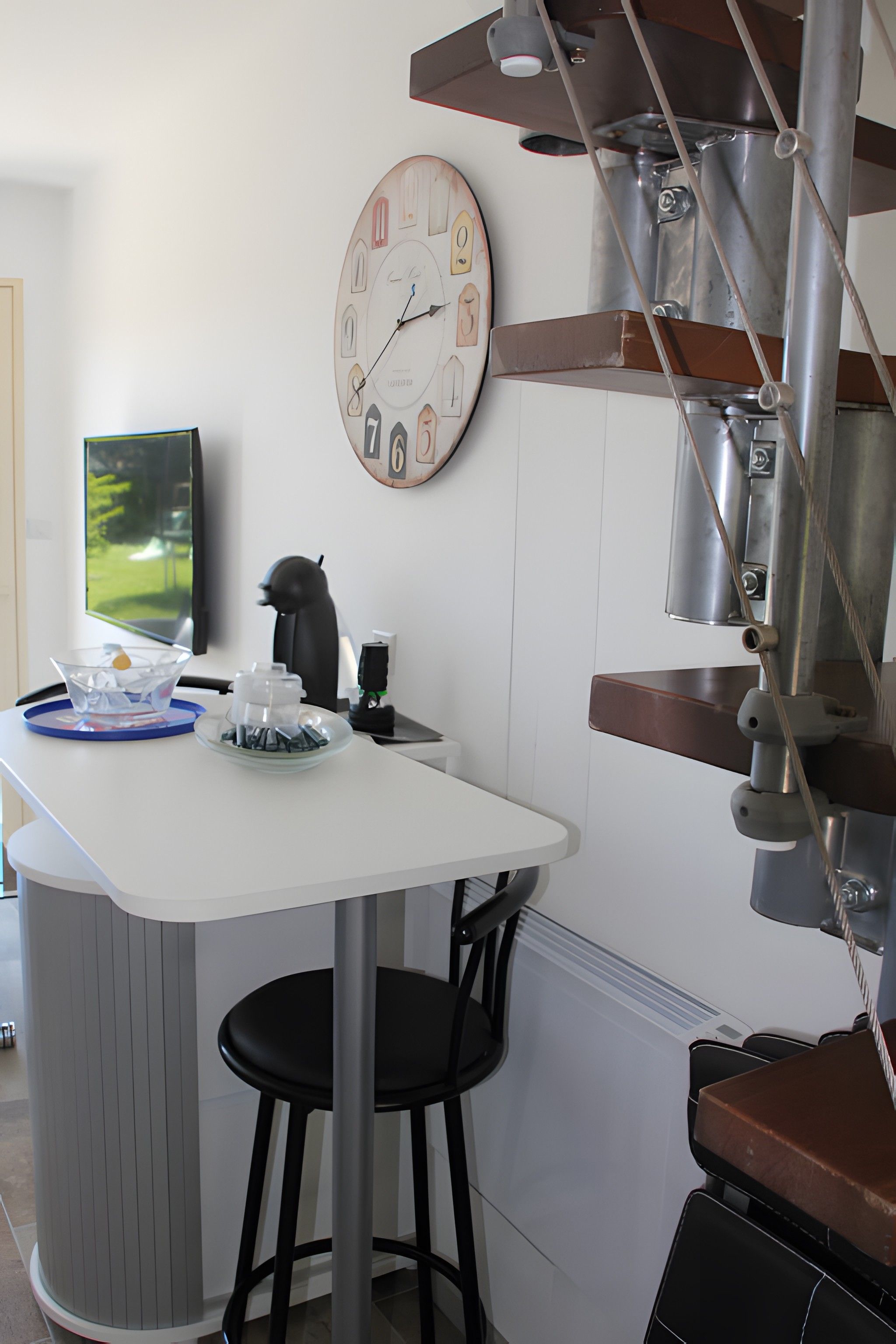 A modern kitchen with a white countertop, a clock, and a coffee machine.