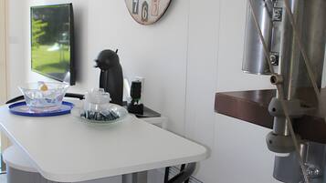 A modern kitchen with a white countertop, a clock, and a coffee machine.
