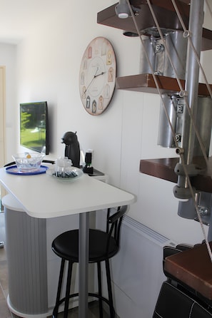 A modern kitchen with a white countertop, a clock, and a coffee machine.