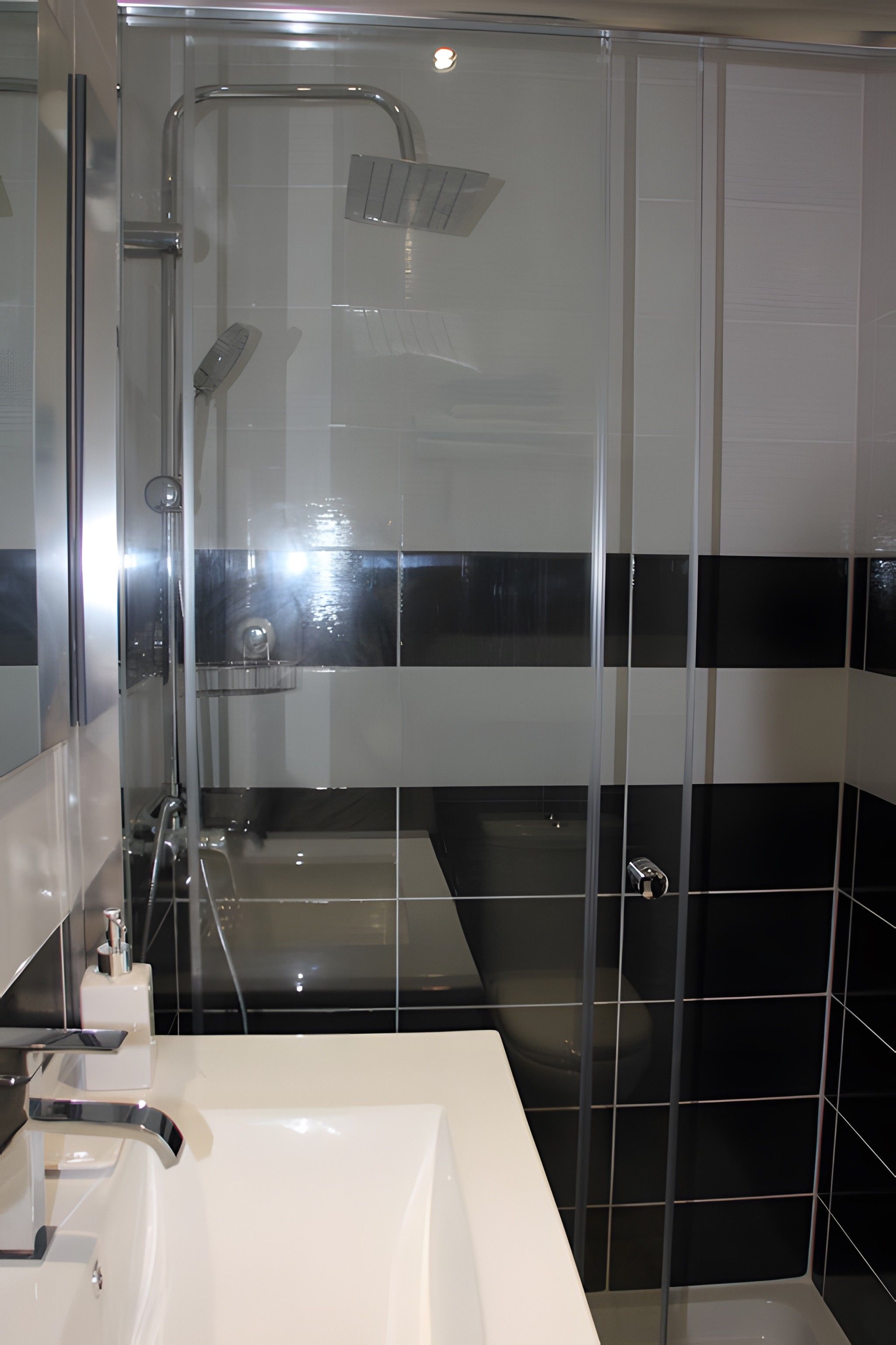 A modern bathroom with a glass shower enclosure, a white sink, and black and white tiled walls.