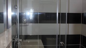 A modern bathroom with a glass shower enclosure, a white sink, and black and white tiled walls.
