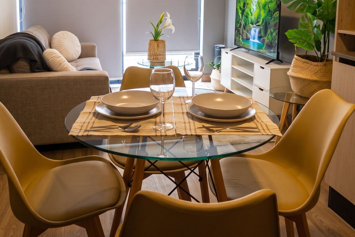A modern living room with a dining area, a sofa, a TV, and a large window.