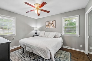 Quarto com cama, ventoinha no teto, mesa de cabeceira com abajur e janela com persianas.