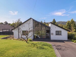 A modern two-story house with a large glass window, a small tree in the front yard, and a clear sky. - Rayrigg on the Lakes (Windermere)