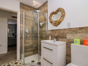 A bathroom with a glass-enclosed shower, a white sink with a mirror above it, and a wooden wall panel. - Rayrigg on the Lakes (Windermere)