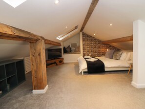A loft bedroom with a sloped ceiling, a television, a sofa, and a patterned wall. - Rayrigg on the Lakes (Windermere)